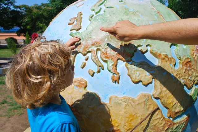 A young child looks at a large globe whilst an adult points to Europe on the globe.
